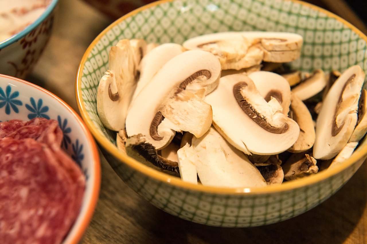 A bowl filled with sliced white mushrooms, with a bowl of sliced meat partially visible beside it.