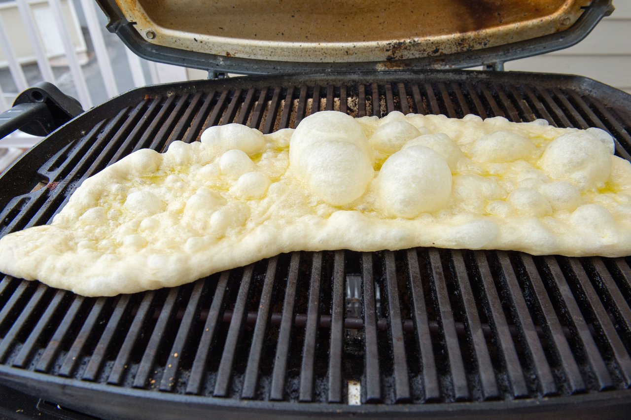 Uncooked pizza dough with bubbles forming as it cooks on a grill.