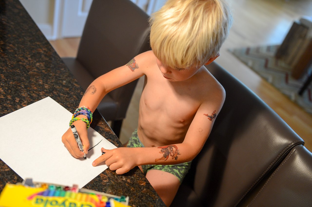 A young boy sits at a table, drawing on a blank sheet of paper with a marker.