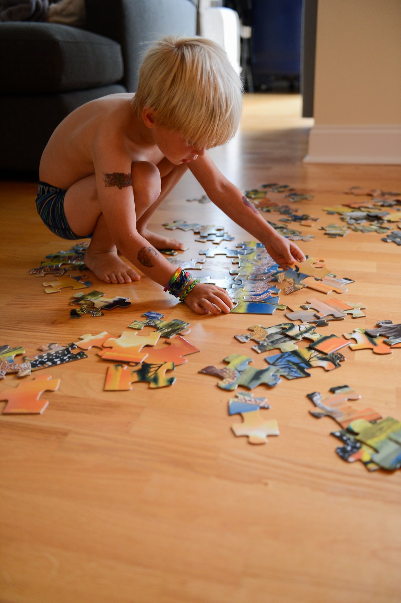 A young child sits on the floor, carefully assembling a large puzzle with scattered pieces around them.