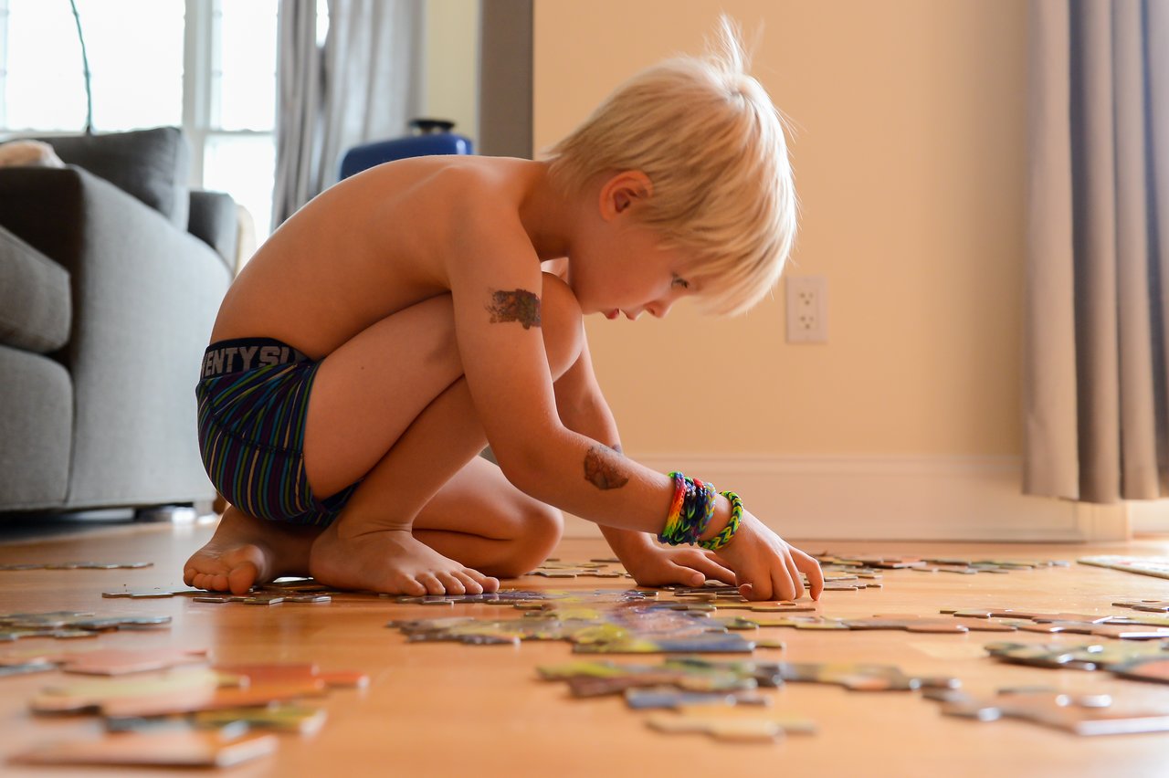 A young boy crouches on the floor, focused on assembling a large puzzle with scattered pieces around him.