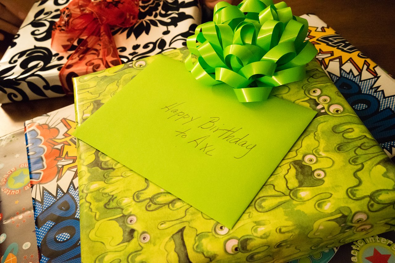A stack of wrapped birthday presents with a green envelope labeled "Happy Birthday to Axl" on top.
