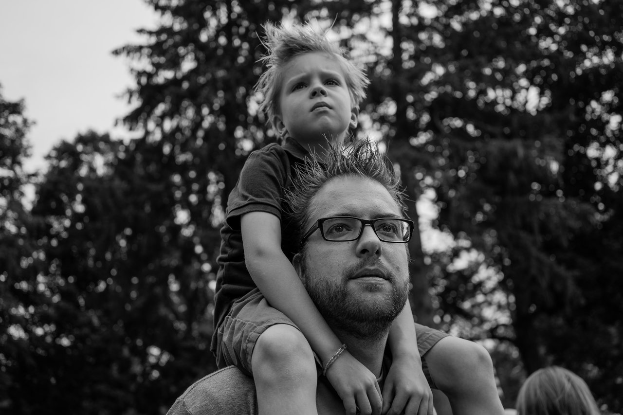 A man carries a young boy on his shoulders as they both look into the distance.