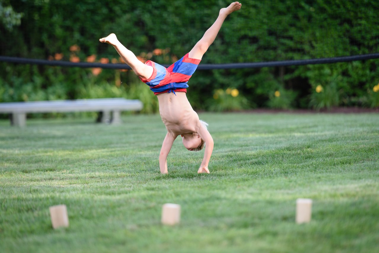 A child in red and blue shorts does a cartwheel on a grassy lawn.