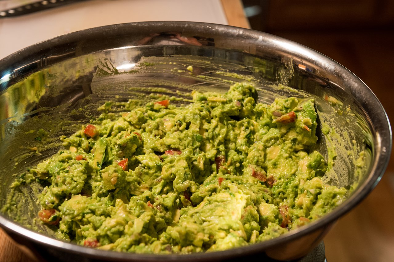 A large metal bowl filled with freshly made guacamole, with chunks of avocado, tomato, and other ingredients mixed in.