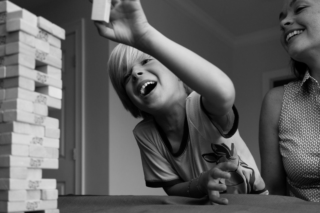 A child excitedly removes a Jenga block while an adult smiles beside them during a game night.