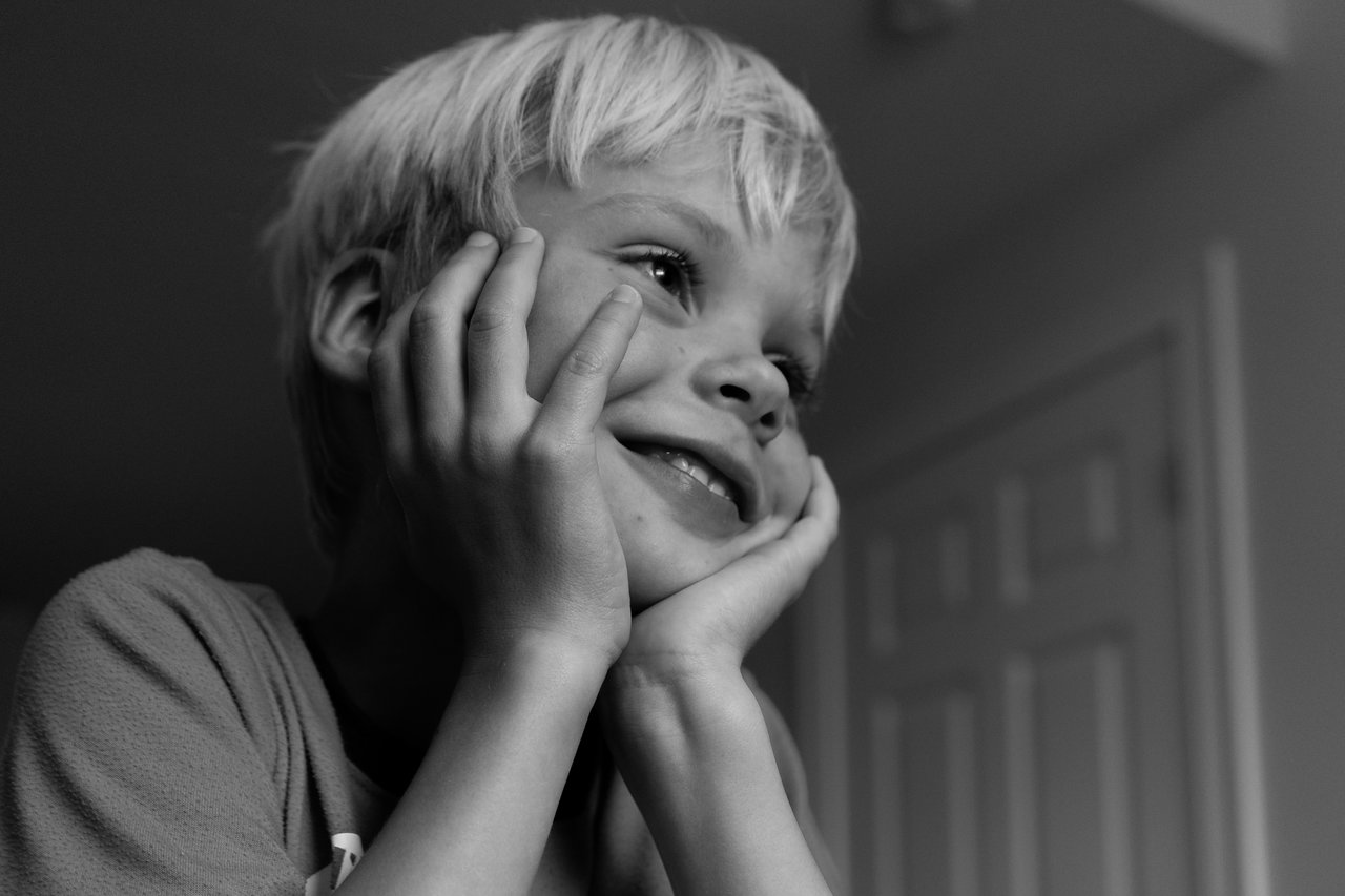 A child smiles and rests their face in their hands, looking at something off-camera during Jenga night.