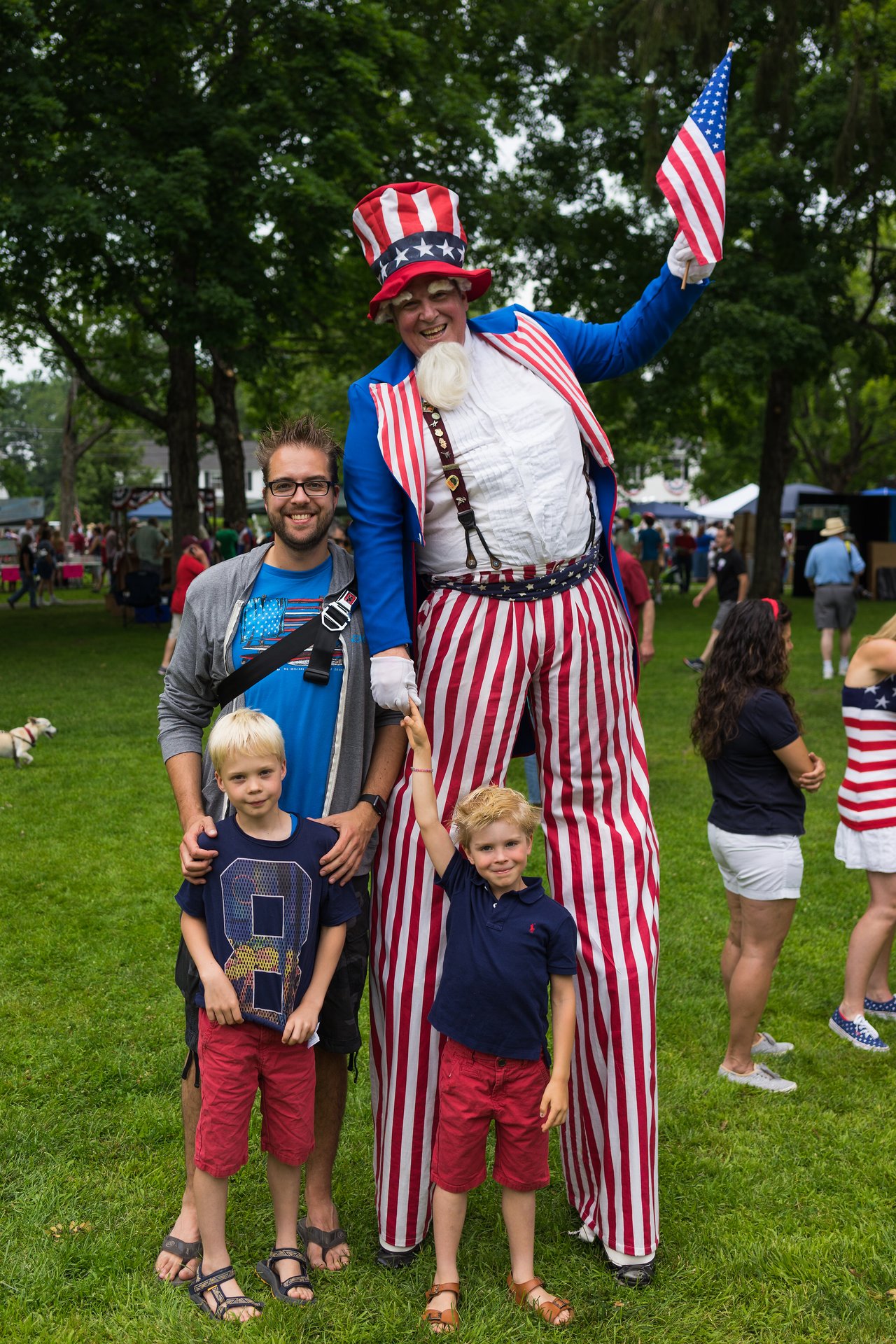 A tall performer dressed as Uncle Sam waves a flag while posing with a smiling man and two young boys.