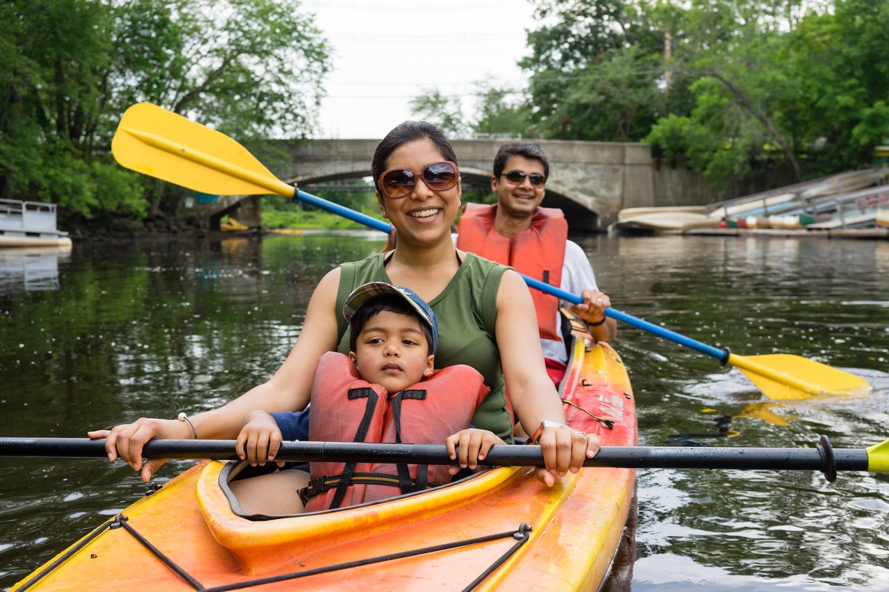 A family kayaking on a calm river, with a woman and child in front and a man paddling behind them.