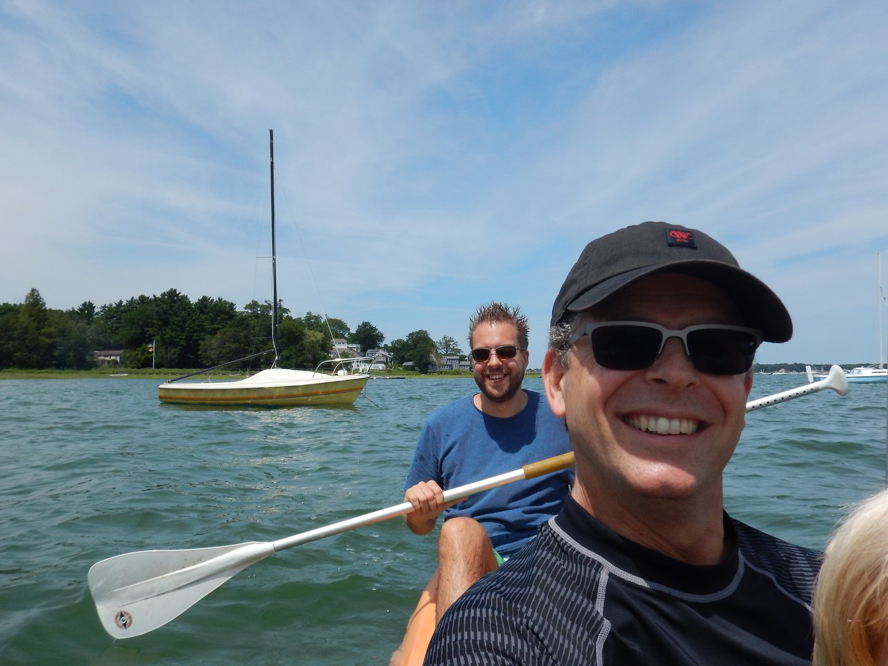 Two people in a kayak smiling, with one holding a paddle on a sunny day near the water.