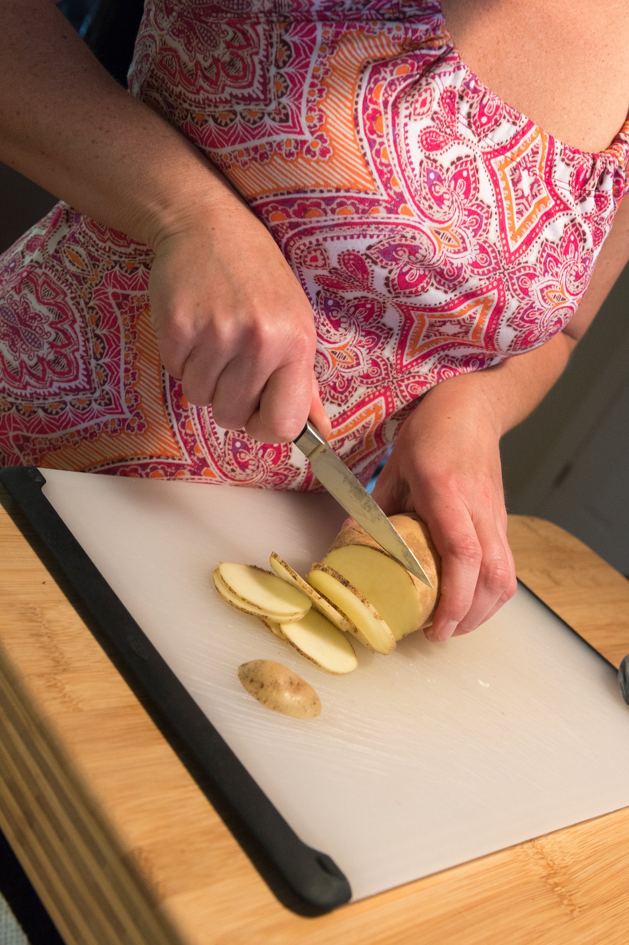 A person slices a potato on a white cutting board using a knife.