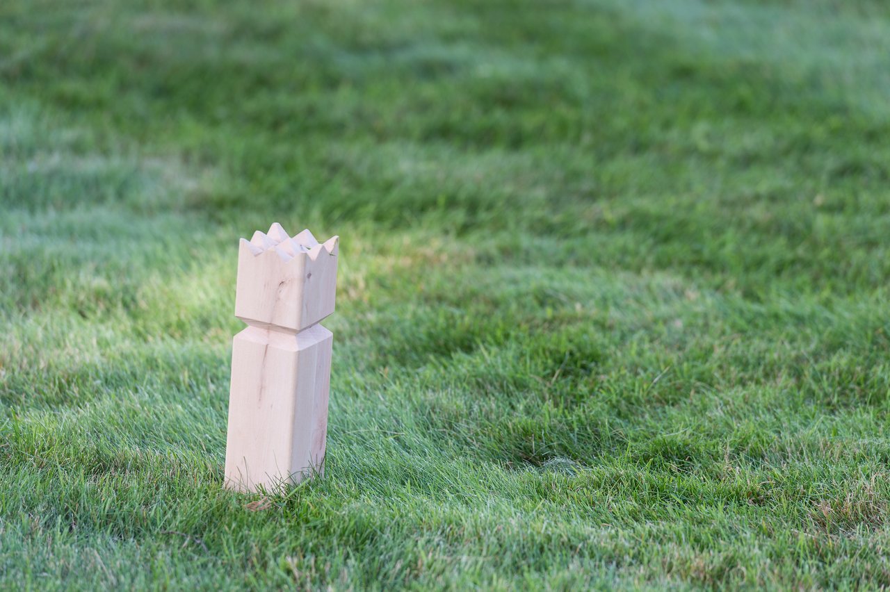 A wooden kubb king piece stands on a grassy field, set up for a game of kubb.