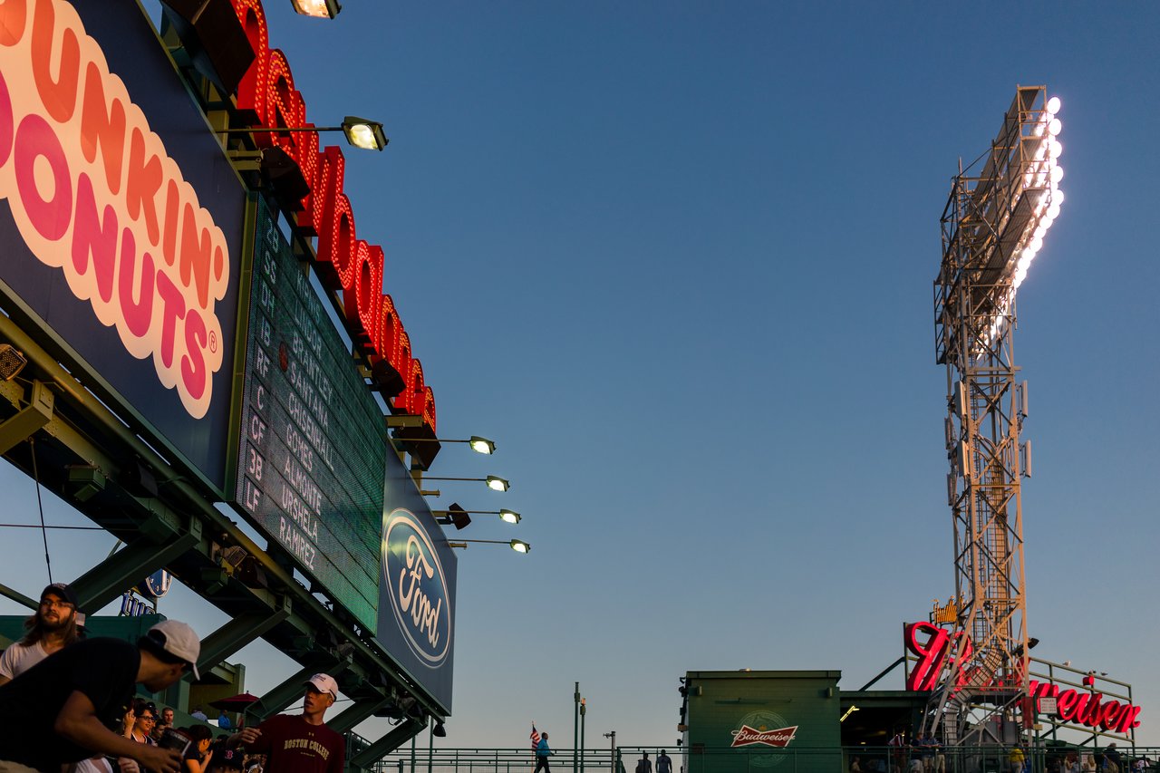 A scoreboard and stadium lights at Fenway Park, with fans gathered in the stands during a Red Sox game.