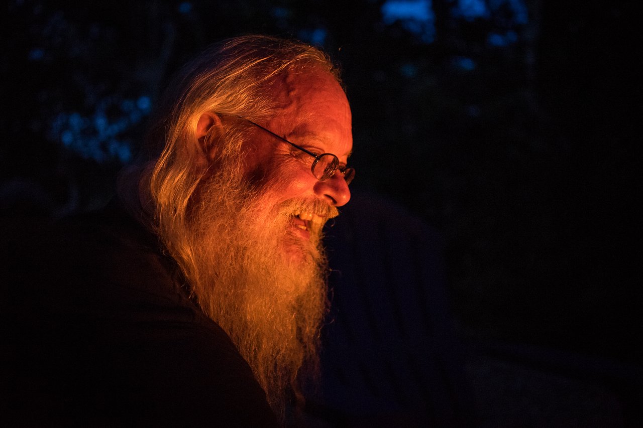 A bearded man smiles near a warm campfire at night, likely making s'mores at Cape Cod.