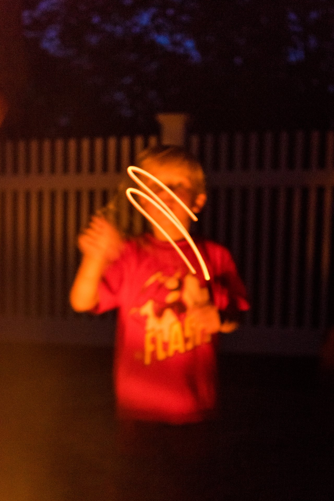 A child in a red shirt waves a glowing object near a fire at night.