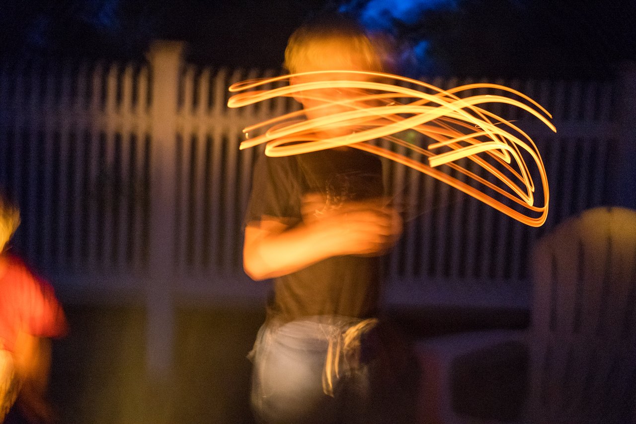 A person moves a glowing object at night, creating light trails in the air.