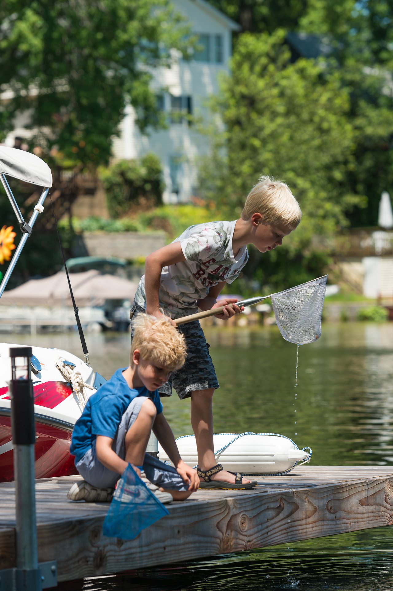 Two boys on a wooden dock use nets to catch something from the water on a sunny day.