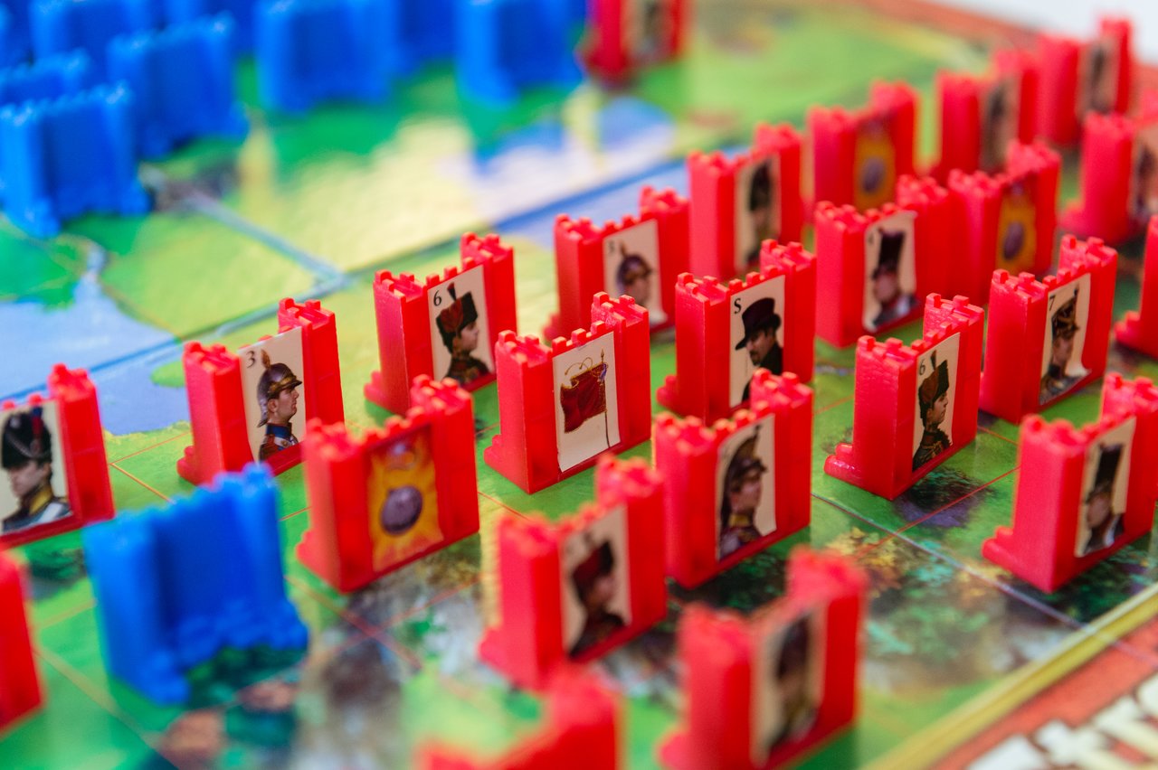 A Stratego board with red and blue game pieces arranged for play, showing soldiers, bombs, and other ranks.