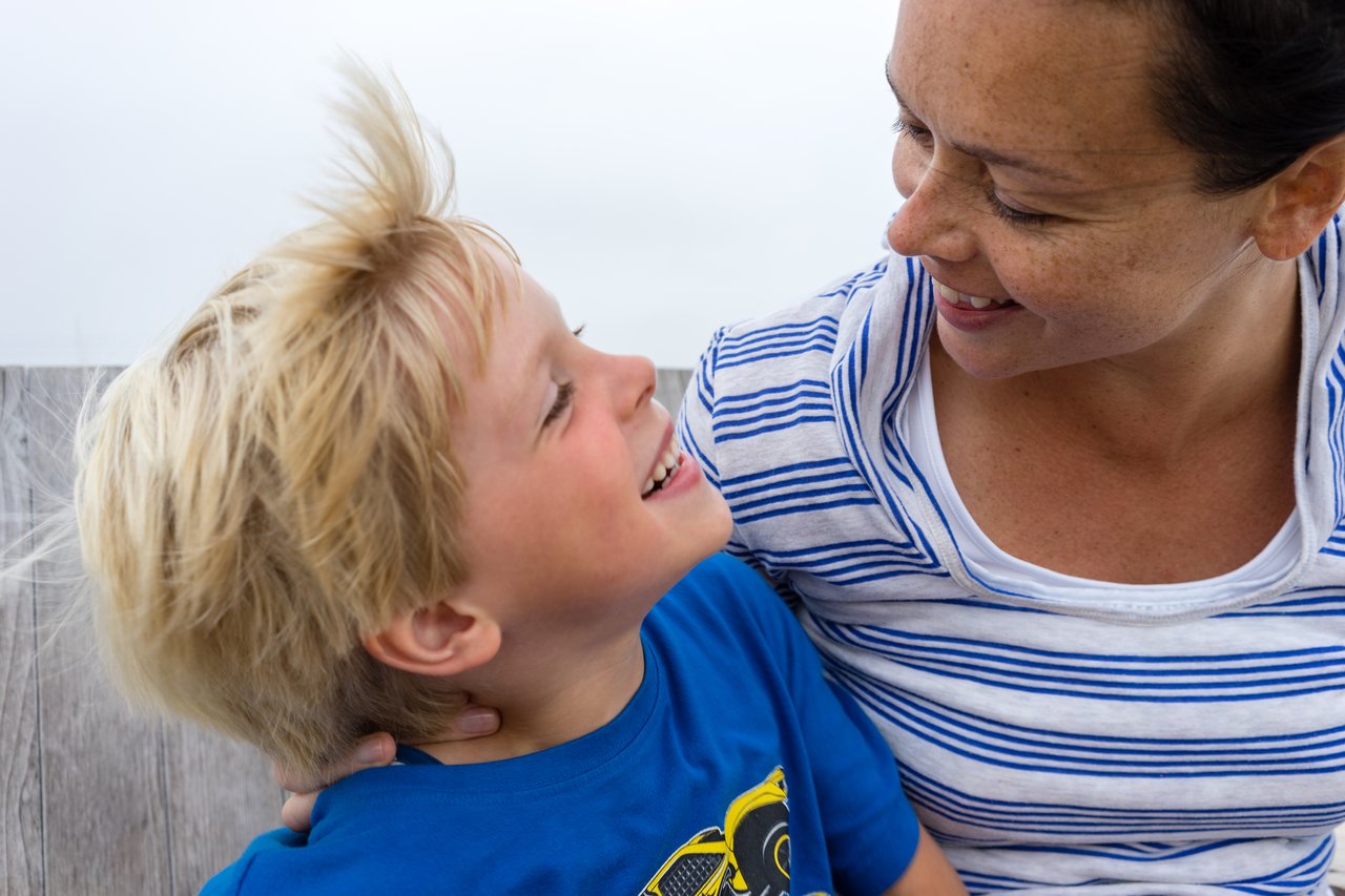 A woman and a young boy smile at each other while sitting together, sharing a happy moment.