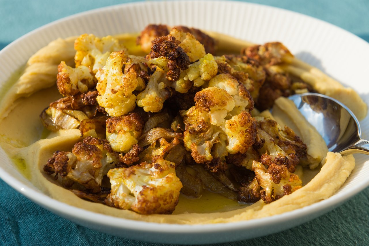 A plate of roasted cauliflower and caramelized onions on hummus, with a spoon resting on the side.
