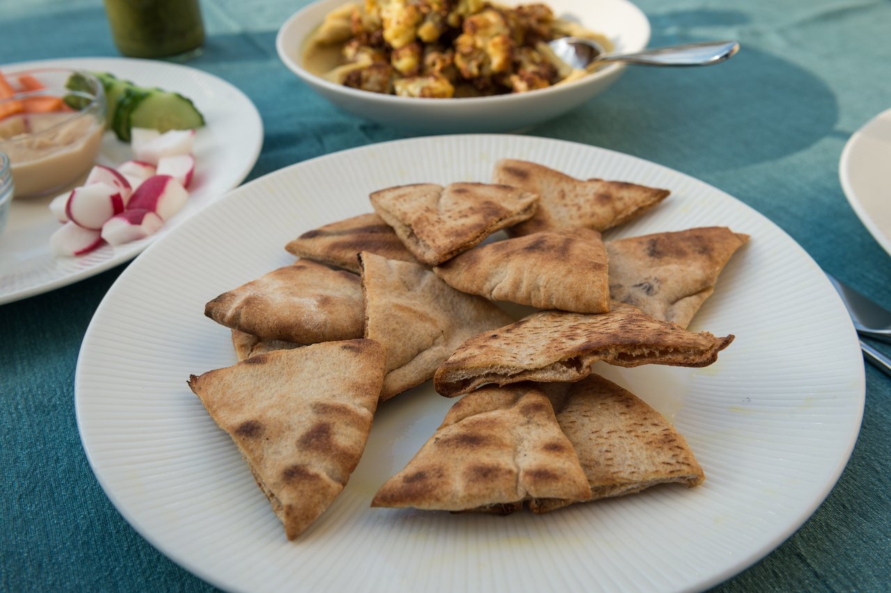 A plate of toasted pita bread slices on a table, with side dishes and a bowl of food in the background.