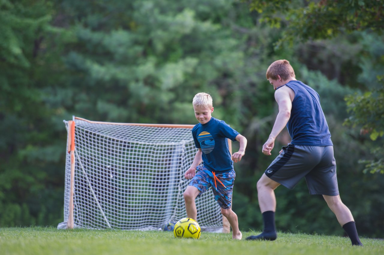 A young boy named Axl plays soccer barefoot, dribbling the ball while an older player tries to defend.