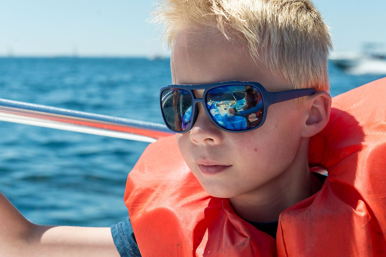 A child wearing sunglasses and a life jacket sits on a boat.
