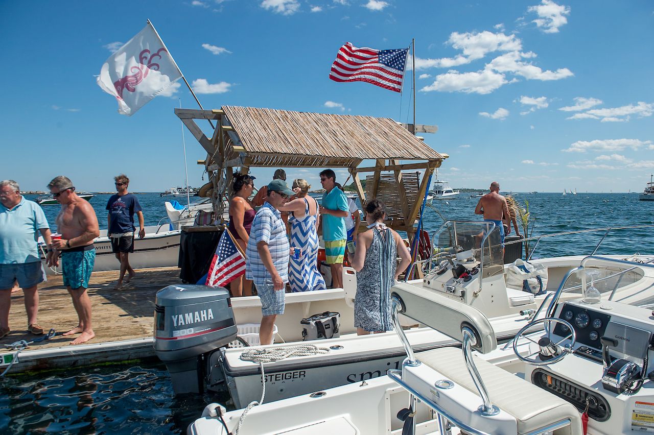 A group of people gathers on a dock, chatting and preparing to board boats on a sunny day.
