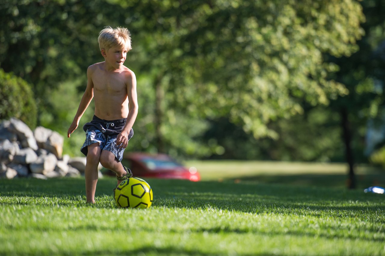 A young boy dribbles a yellow soccer ball on a grassy field during daytime.