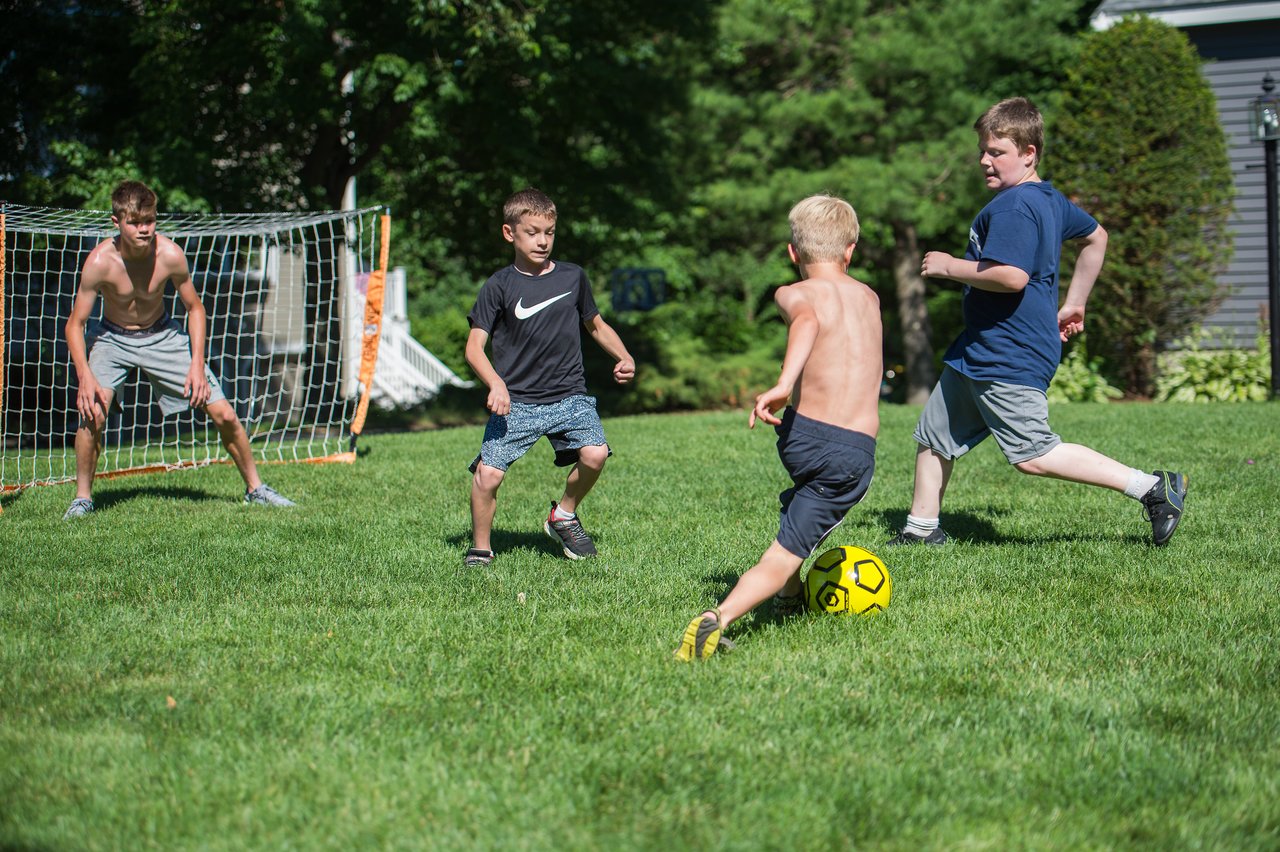 A group of boys play soccer on a grassy field, with Stan dribbling the ball while others defend.