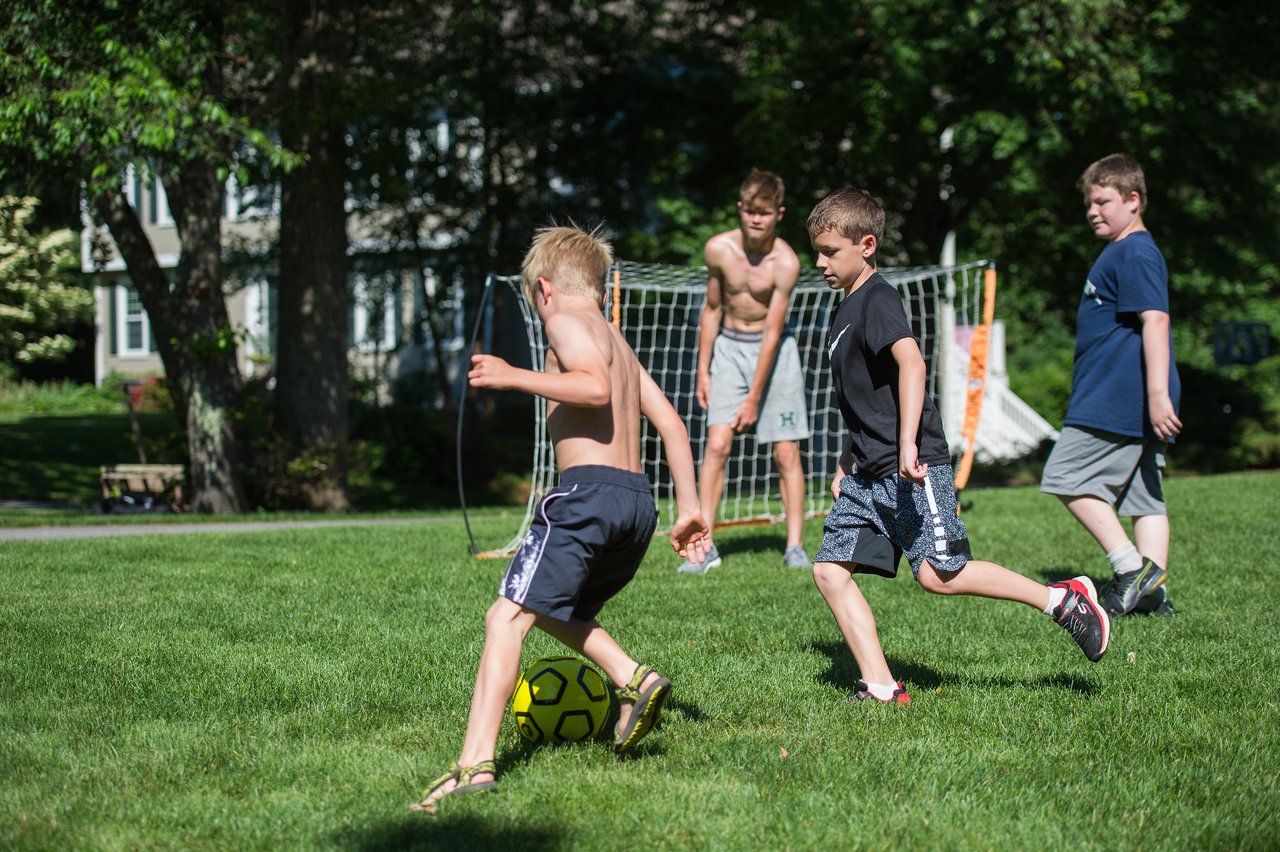 A group of boys play soccer on a grassy field, with Stan controlling the ball while others chase him.