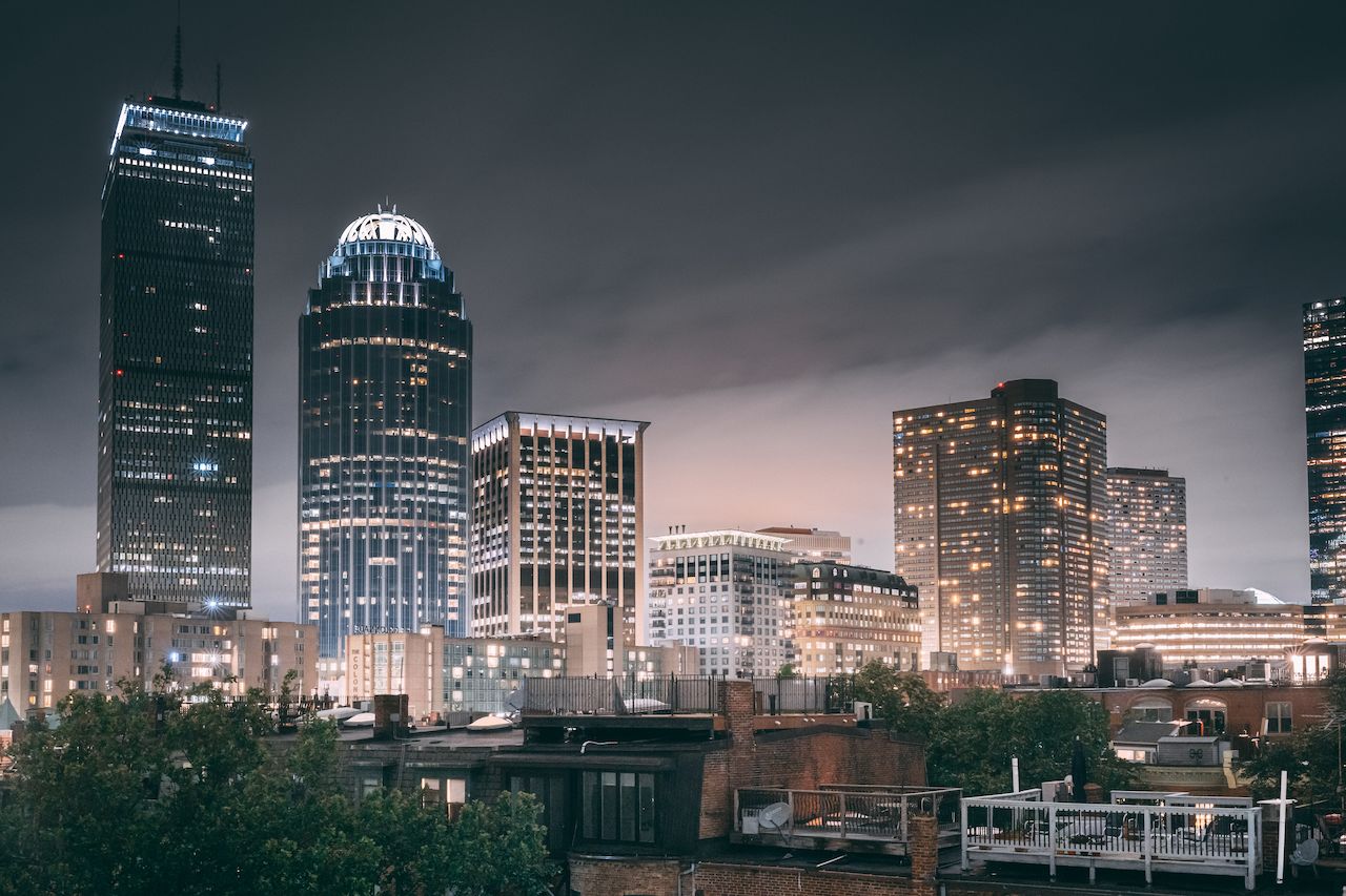 Boston skyline at night with illuminated buildings and rooftops, viewed from a distance.