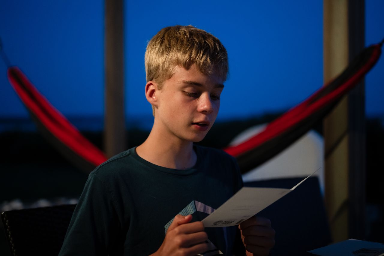 A young person reads a birthday card while sitting outside in the evening.