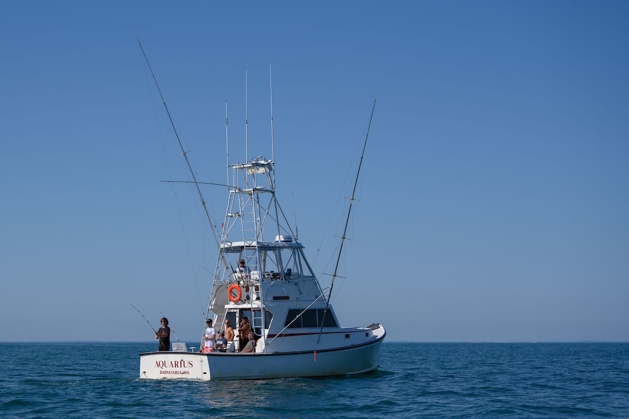 A group of people on a fishing boat, with one person actively fishing in the open sea.