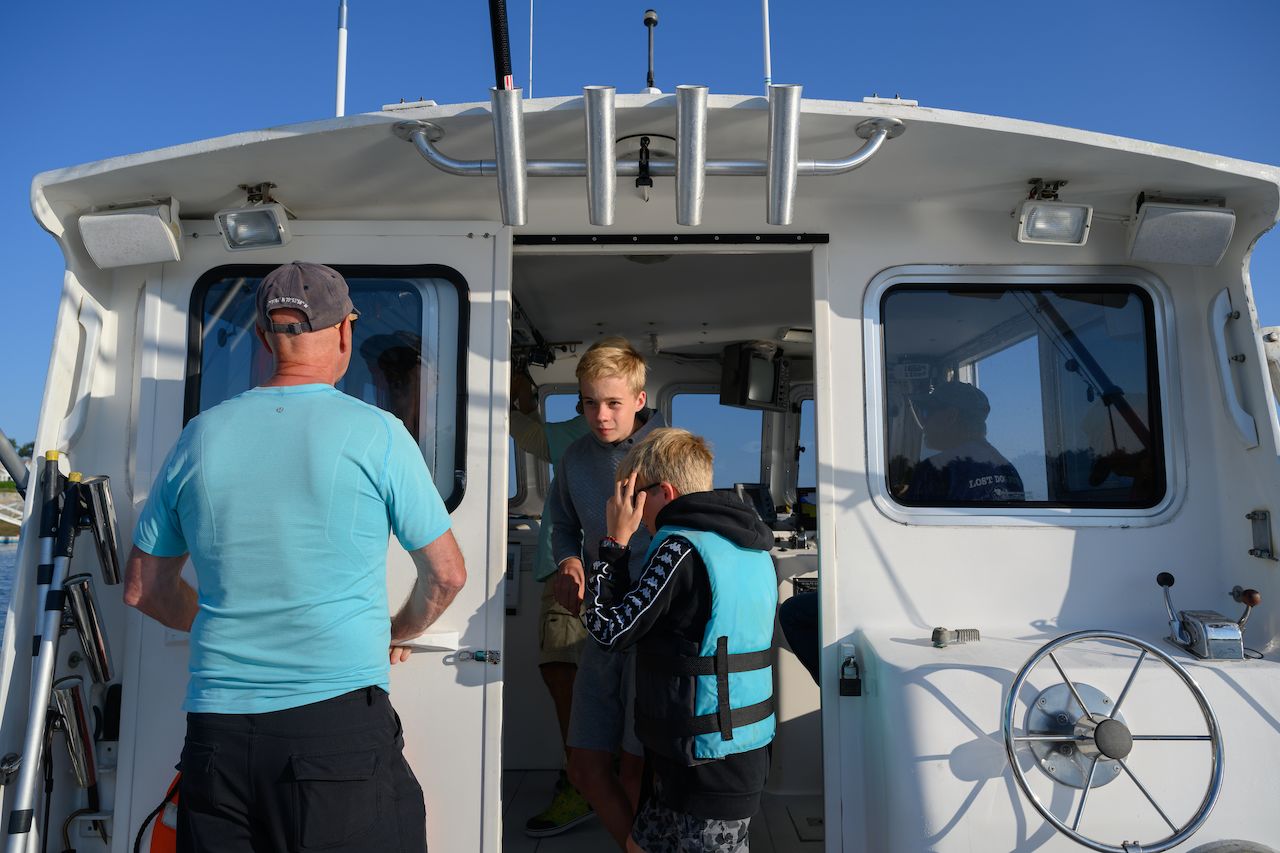 A group of people on a fishing boat, with a child wearing a life vest and others preparing for the trip.