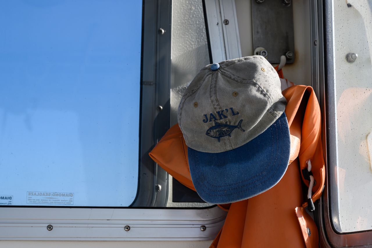 A fishing cap and orange rain gear hang on a boat near a window.