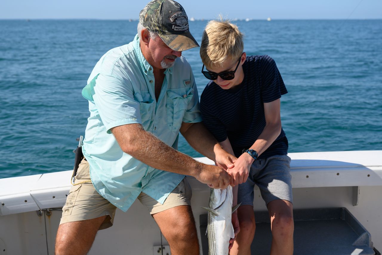 An older man and a young boy work together to hold a freshly caught fish on a boat.
