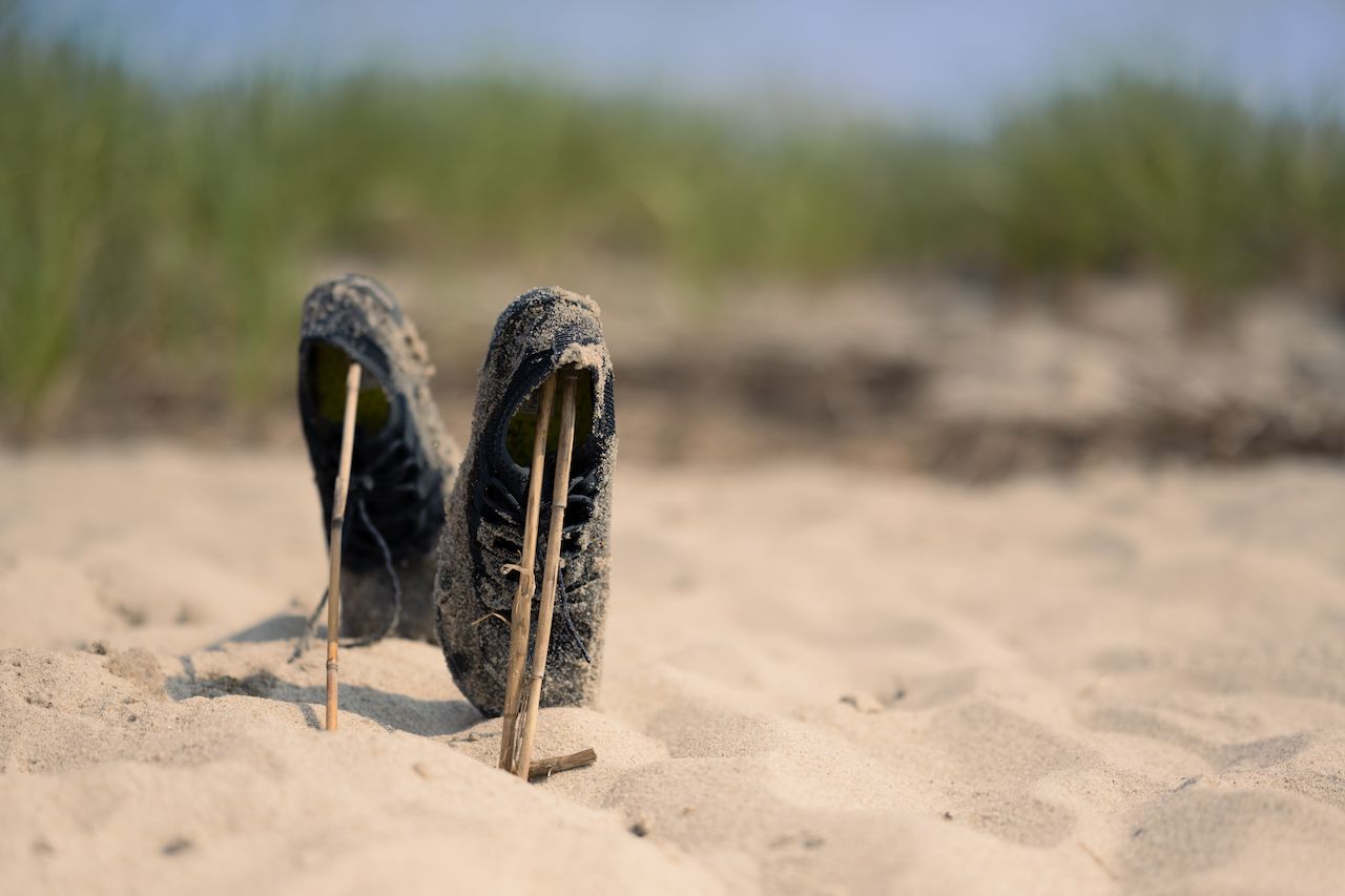 A pair of wet, sandy shoes stand upright on a beach, supported by sticks placed inside them.
