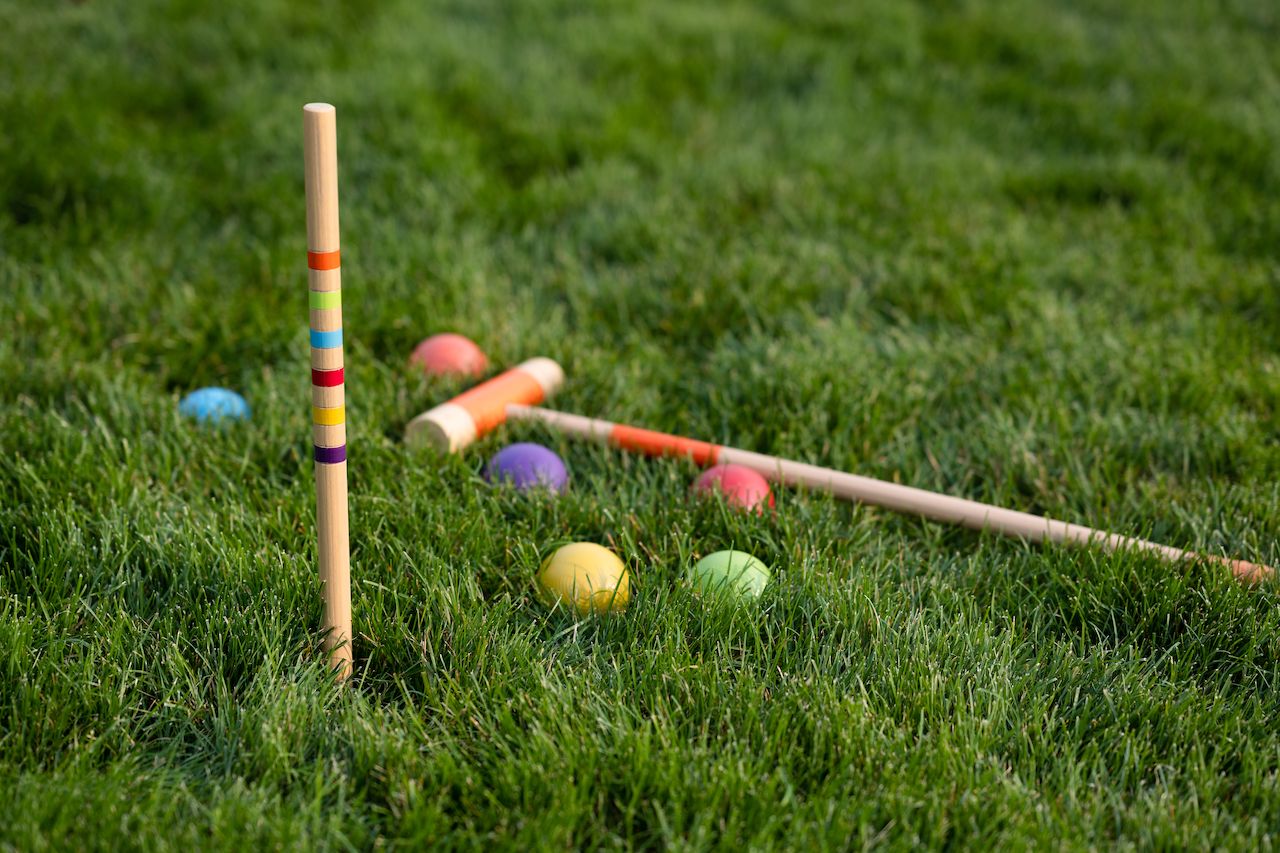 Croquet mallets, balls, and a stake set up on a grassy lawn, ready for a game.