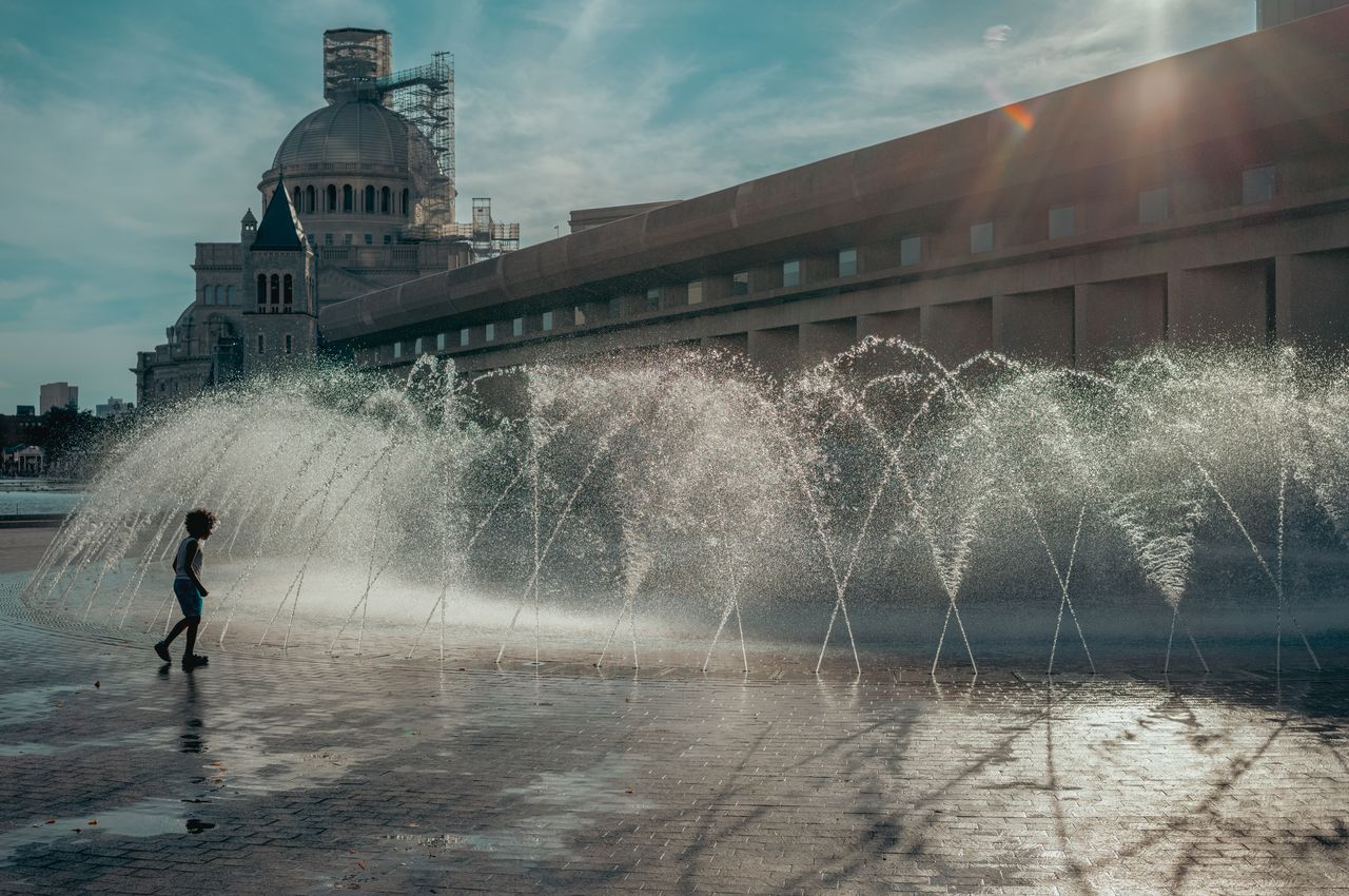 A child plays near arcing water jets in a public fountain at Christian Science Plaza in Boston.