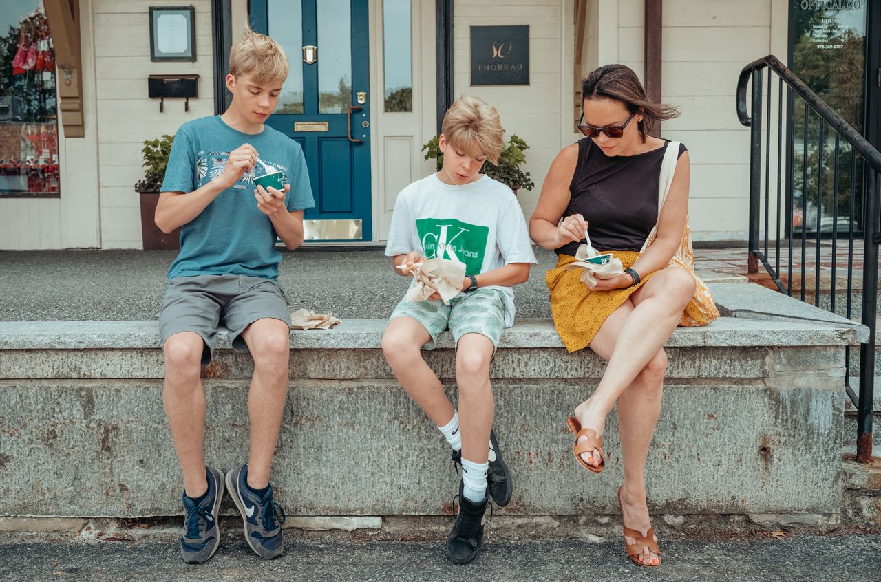 Three people sit on a concrete ledge, eating ice cream from small cups with spoons.