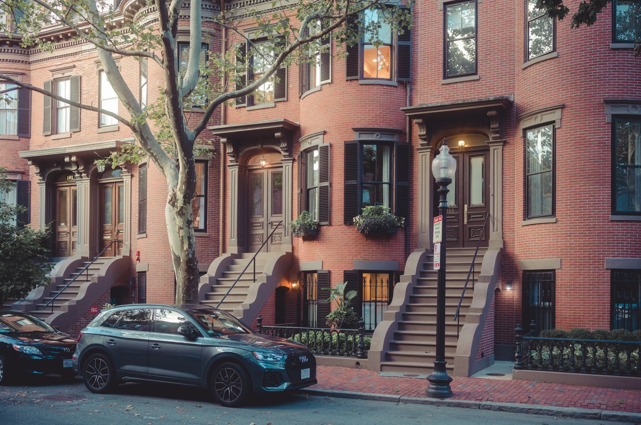 Red brick townhouses with brownstone steps in Boston's South End, with parked cars and a streetlamp in front.