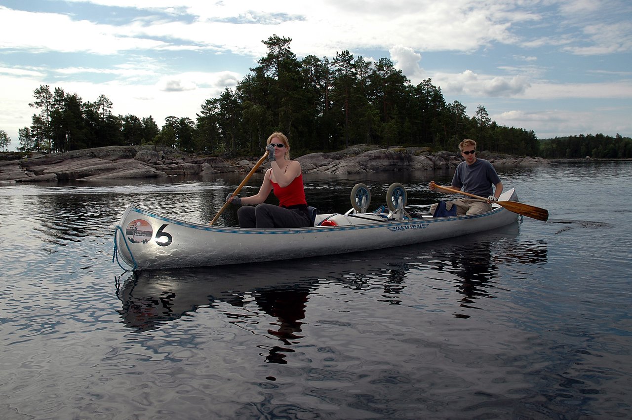 Two people paddling a canoe on calm water, surrounded by rocky shores and trees.