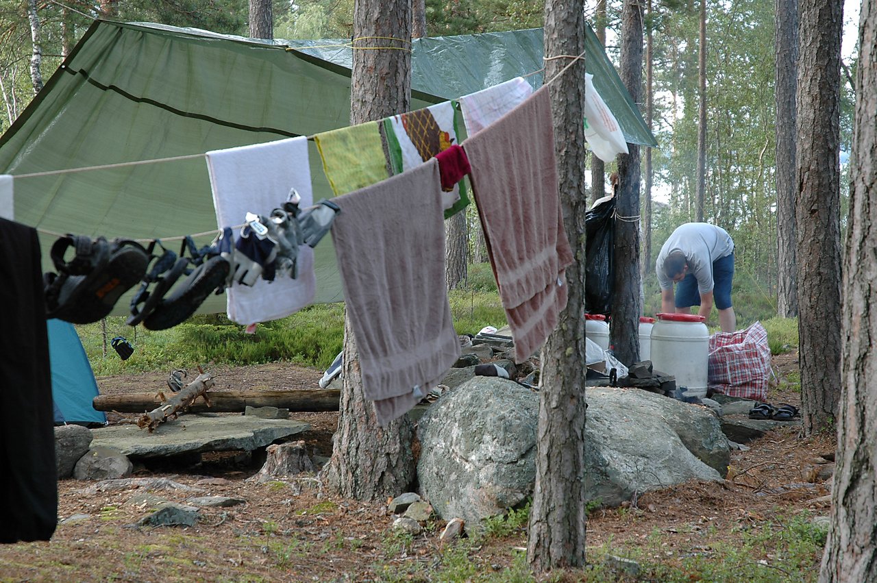 Clothes, towels, and shoes hang on a line to dry at a campsite, while a person works nearby.