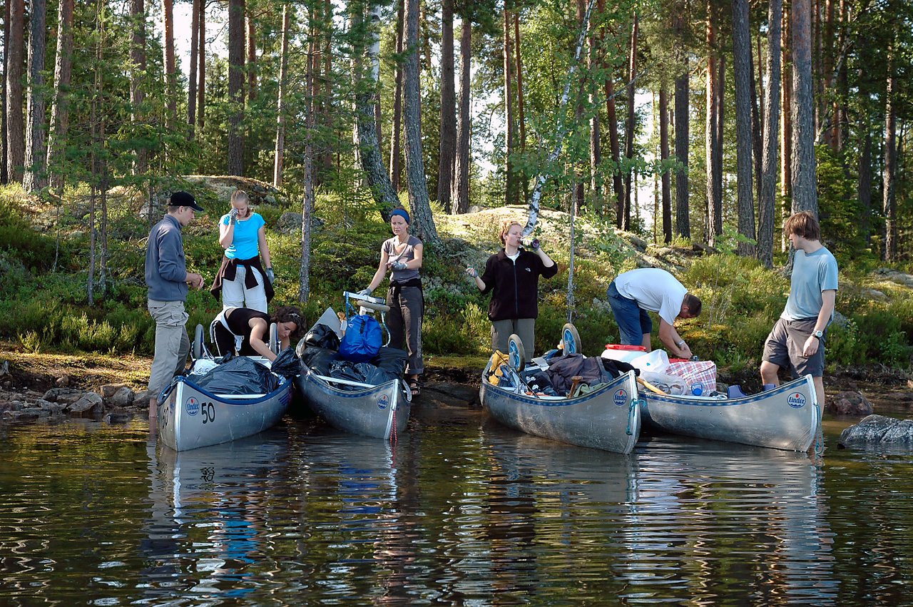 A group of people pack canoes with gear on the shore, preparing for their next trip.