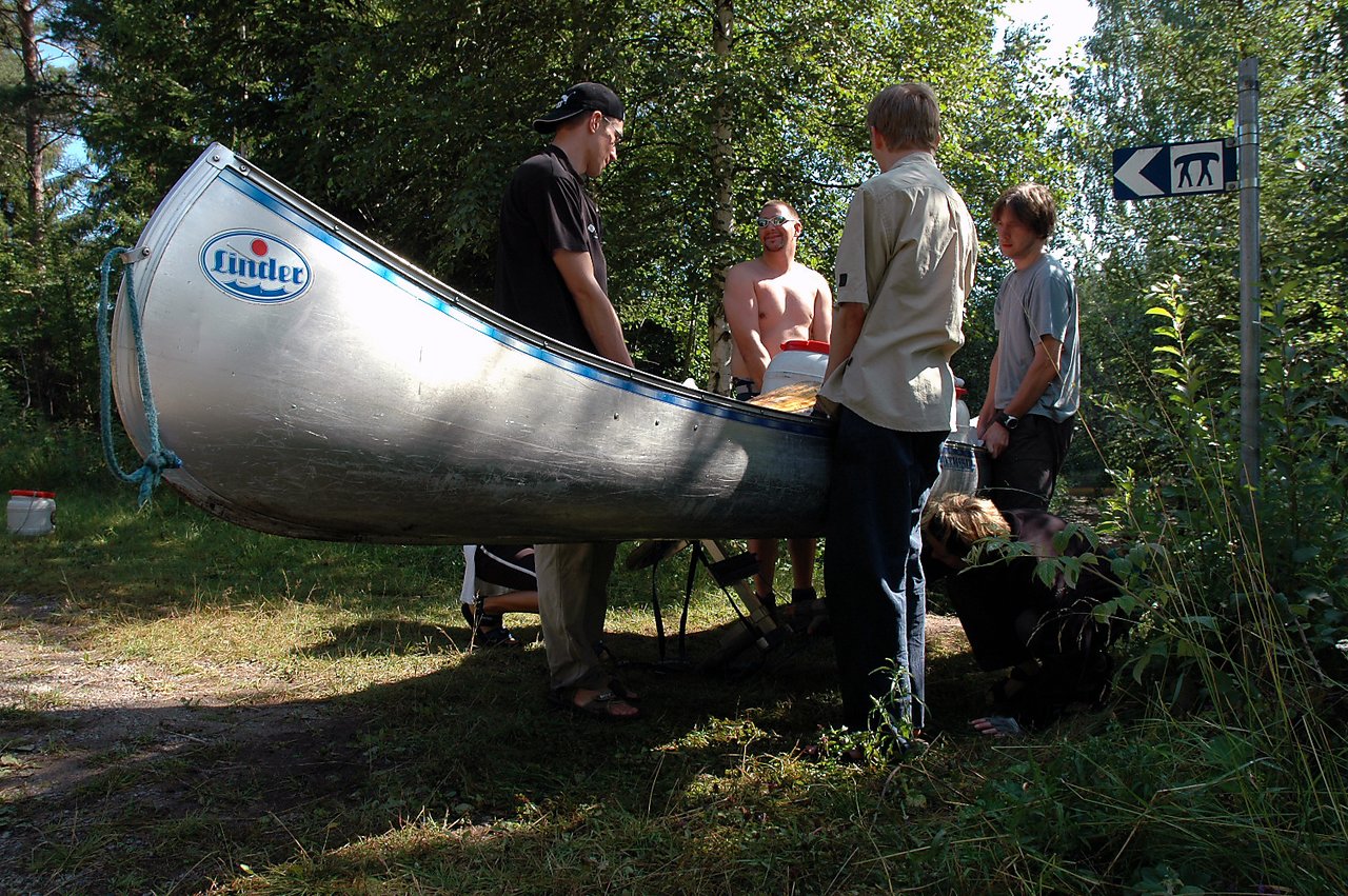 A group of people lifts a canoe to place it onto a small transport wagon for portage.