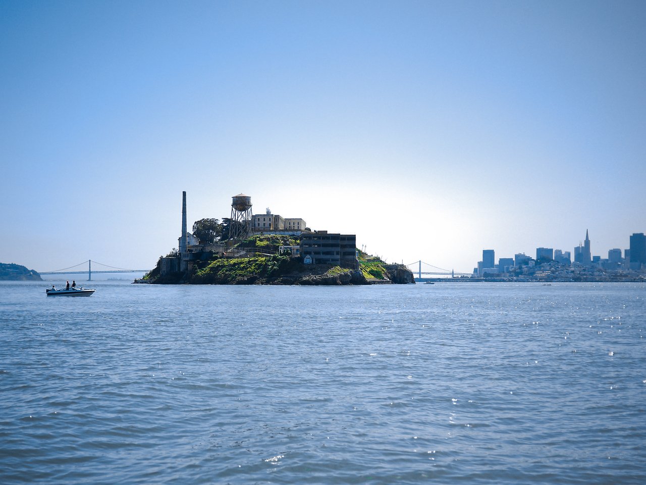 Alcatraz Island with old prison buildings, a water tower, and a boat in the foreground.