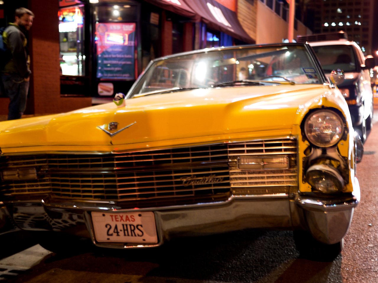 A yellow vintage Cadillac with a damaged front parked on a city street at night.