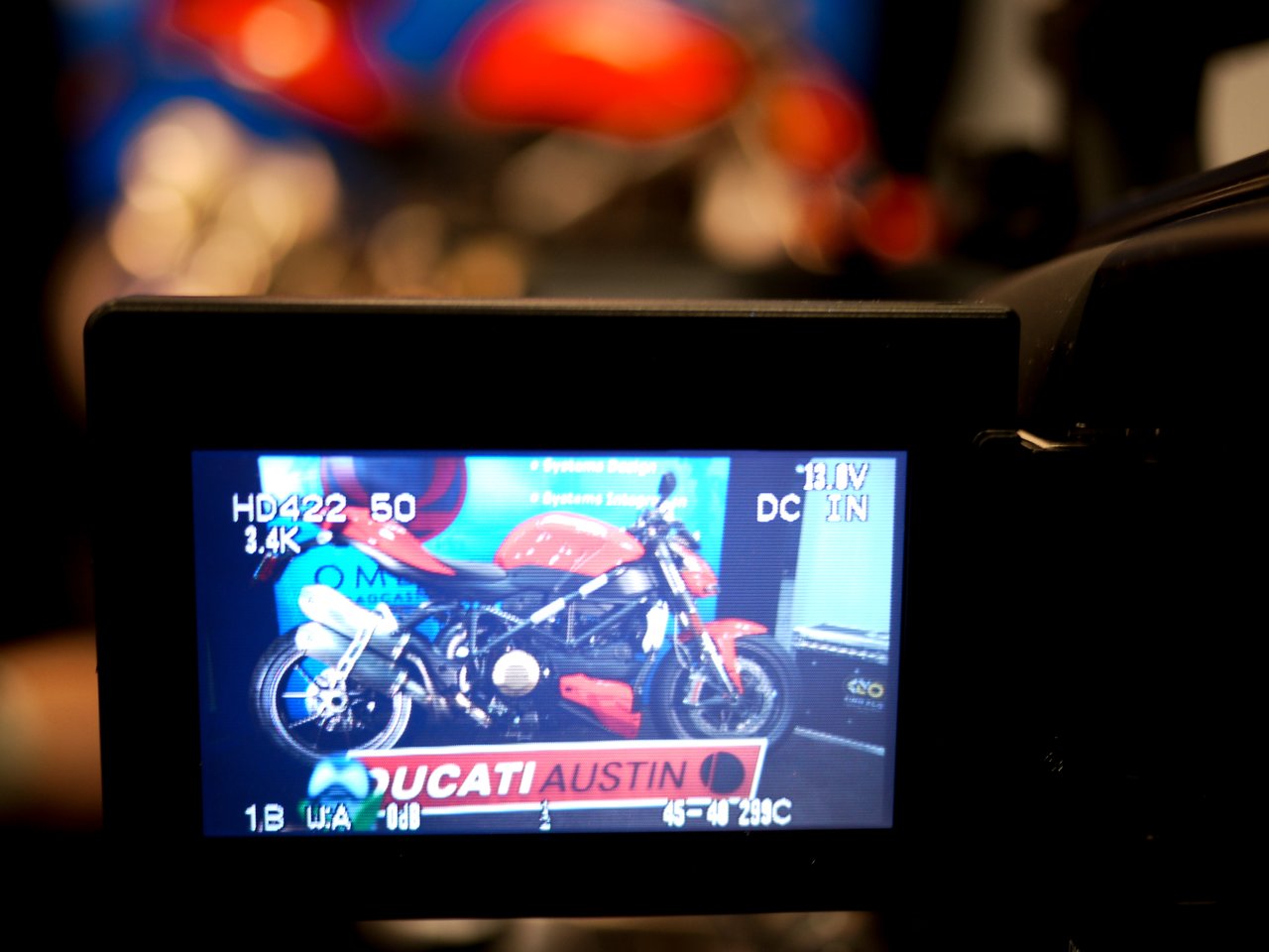 A camera screen displays a red and black motorcycle with a "Ducati Austin" sign in the background.