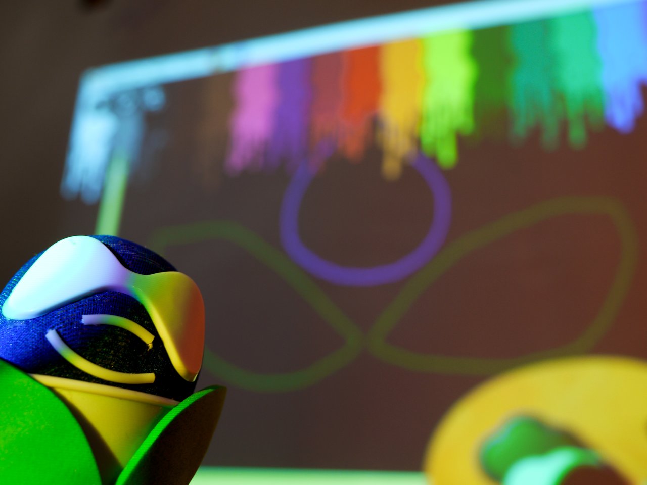 A close-up of a Druplipet figure with a colorful digital painting projected in the background.